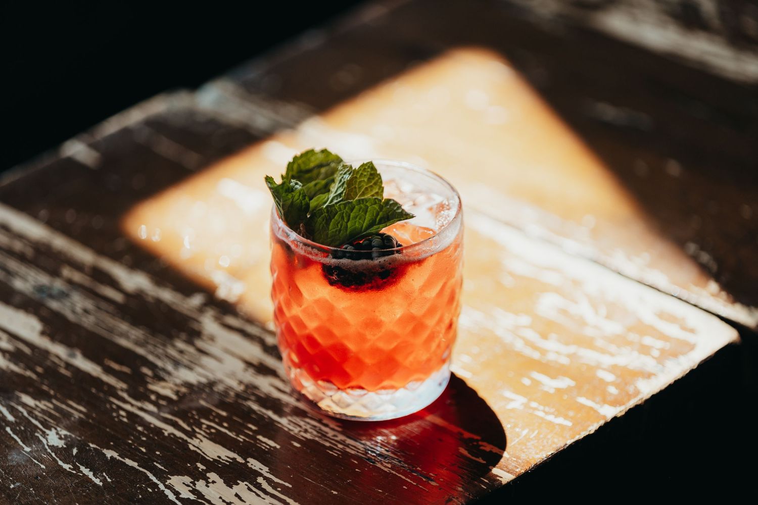 A vibrant red cocktail garnished with mint leaves served on a rustic wooden surface.