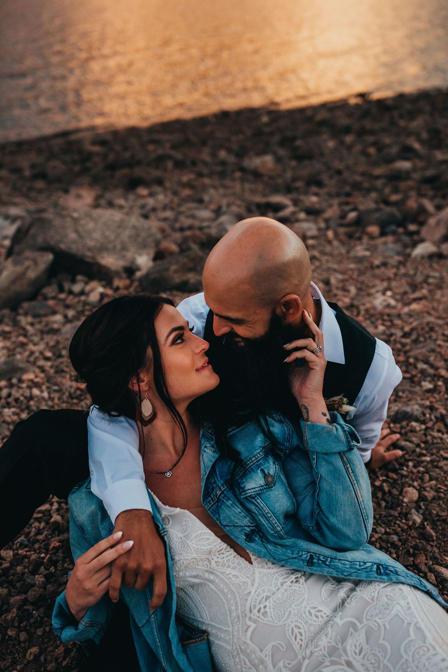 Intimate wedding portrait of couple embracing on rocky shoreline at golden hour.