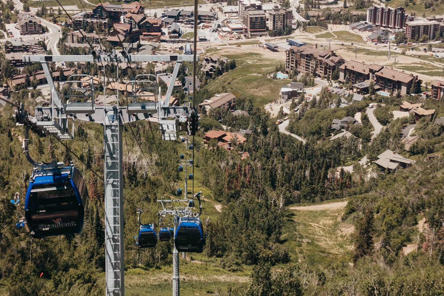 Blue gondola lifts traverse over a mountain resort town with buildings and green slopes visible below.