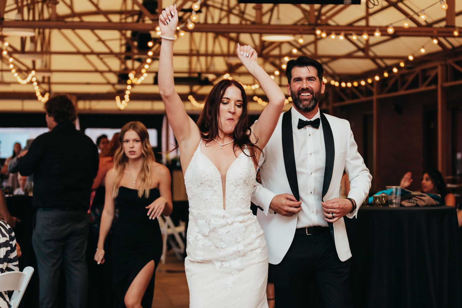 Couple celebrates with raised arms on dance floor at wedding reception.