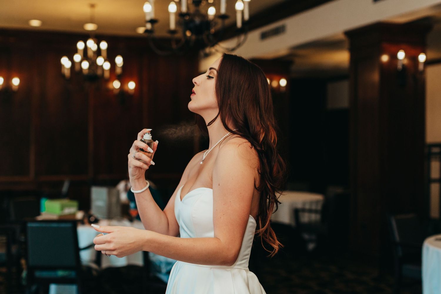 A woman in a white dress singing in an elegant venue with chandeliers.