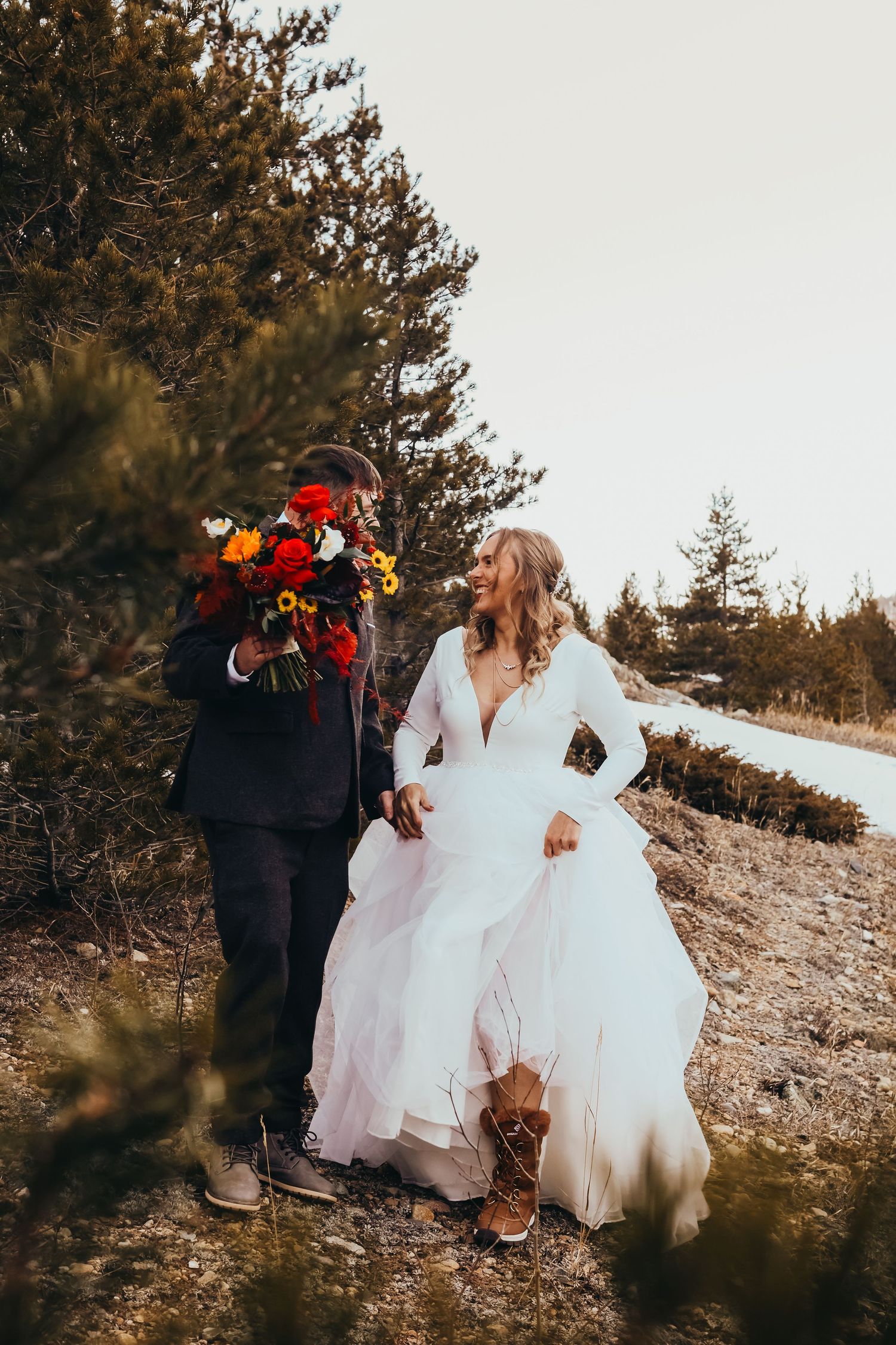 Couple walking through snowy mountain terrain with bright wedding flowers.