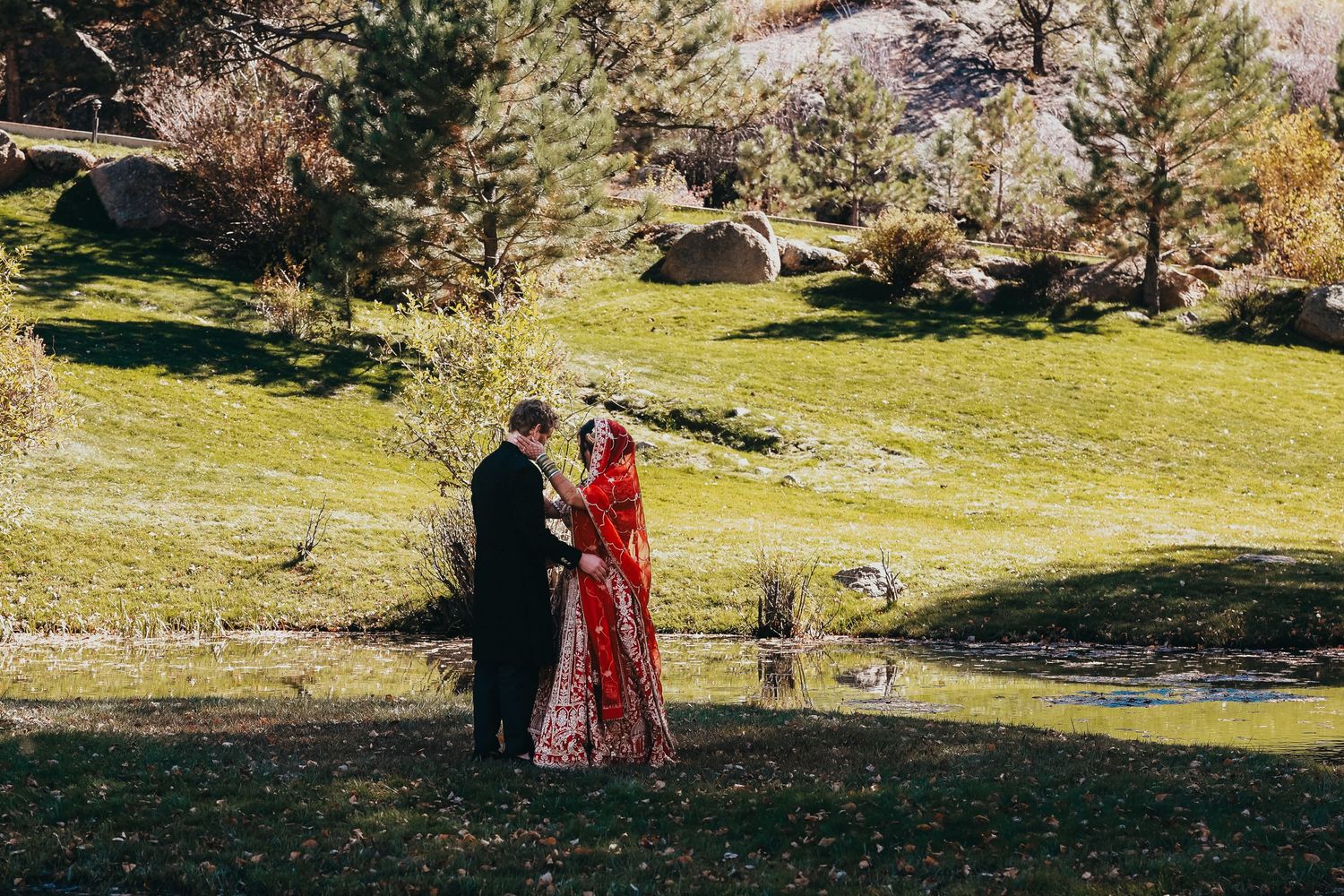 Couple in traditional wedding attire standing together in scenic mountain landscape during autumn.