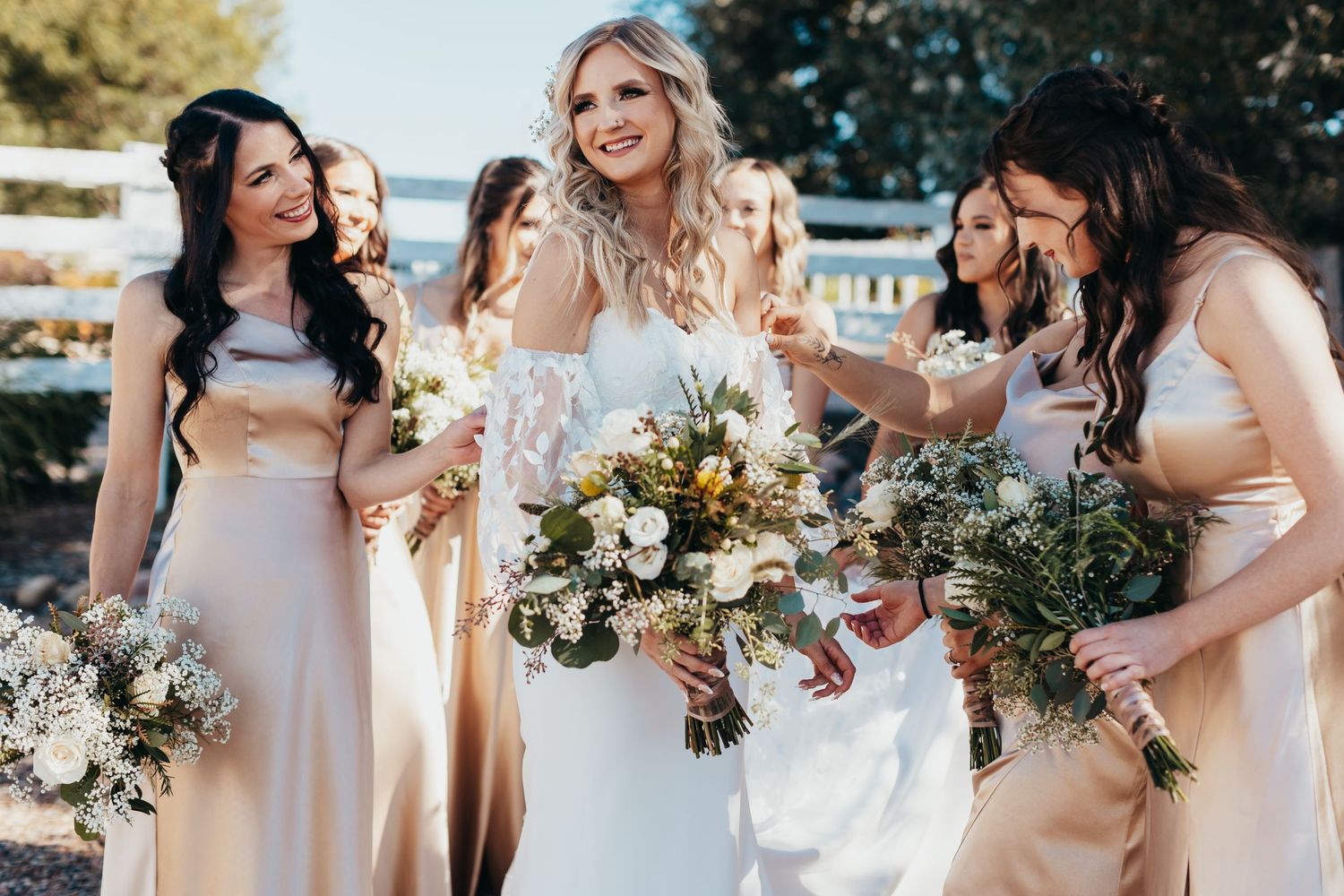 Wedding party laughing together outdoors while holding elegant white and green bouquets.