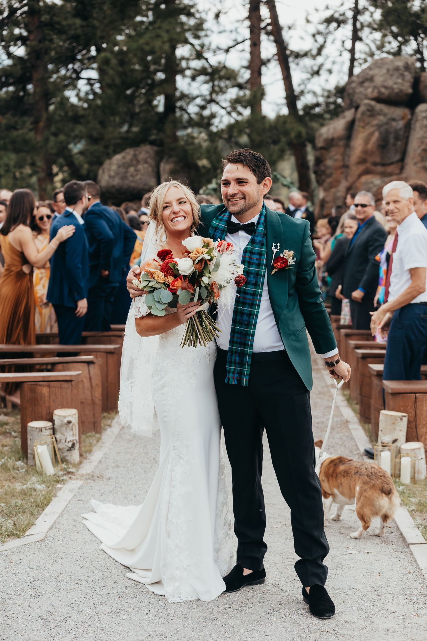 Wedding ceremony in an outdoor forest setting with wooden benches and decorative lanterns lining the aisle.