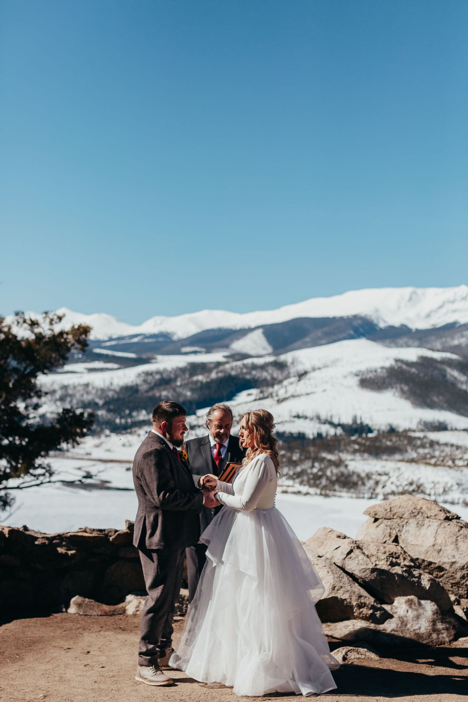 A mountain wedding ceremony with snow-capped peaks and blue skies in the background.