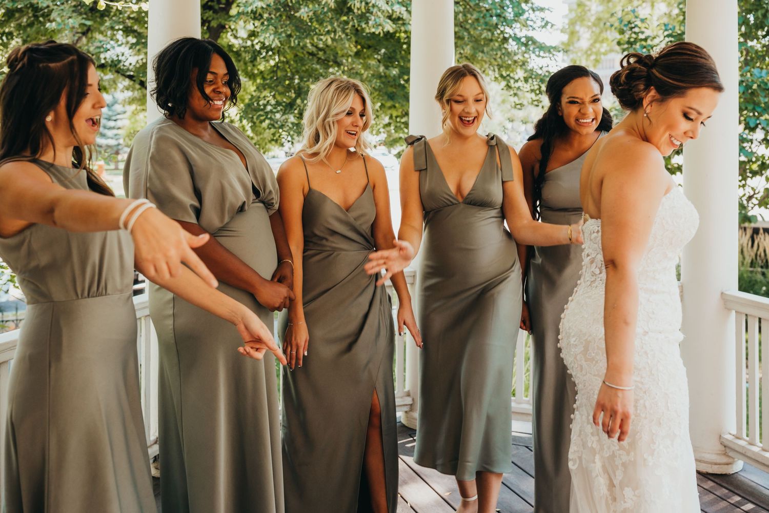 Bridesmaids in matching grey dresses helping with final wedding preparations on a porch.