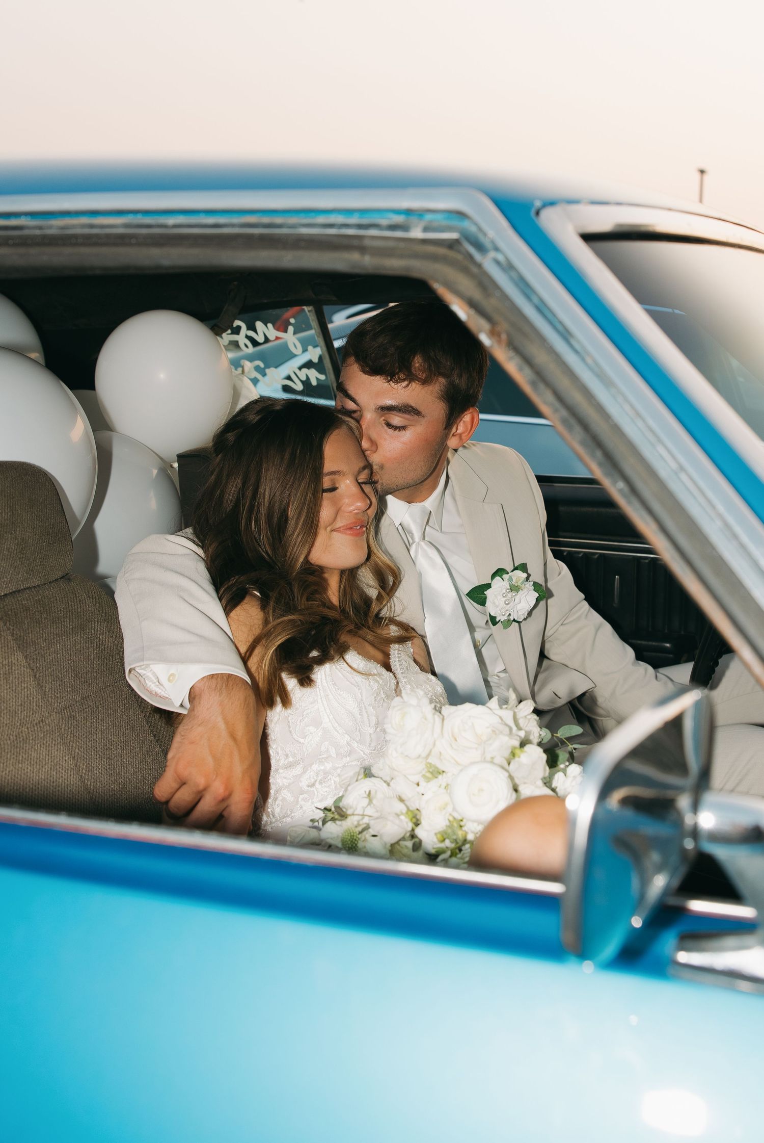 Romantic photo series of newlyweds sharing intimate moments in a vintage blue car with white flowers.