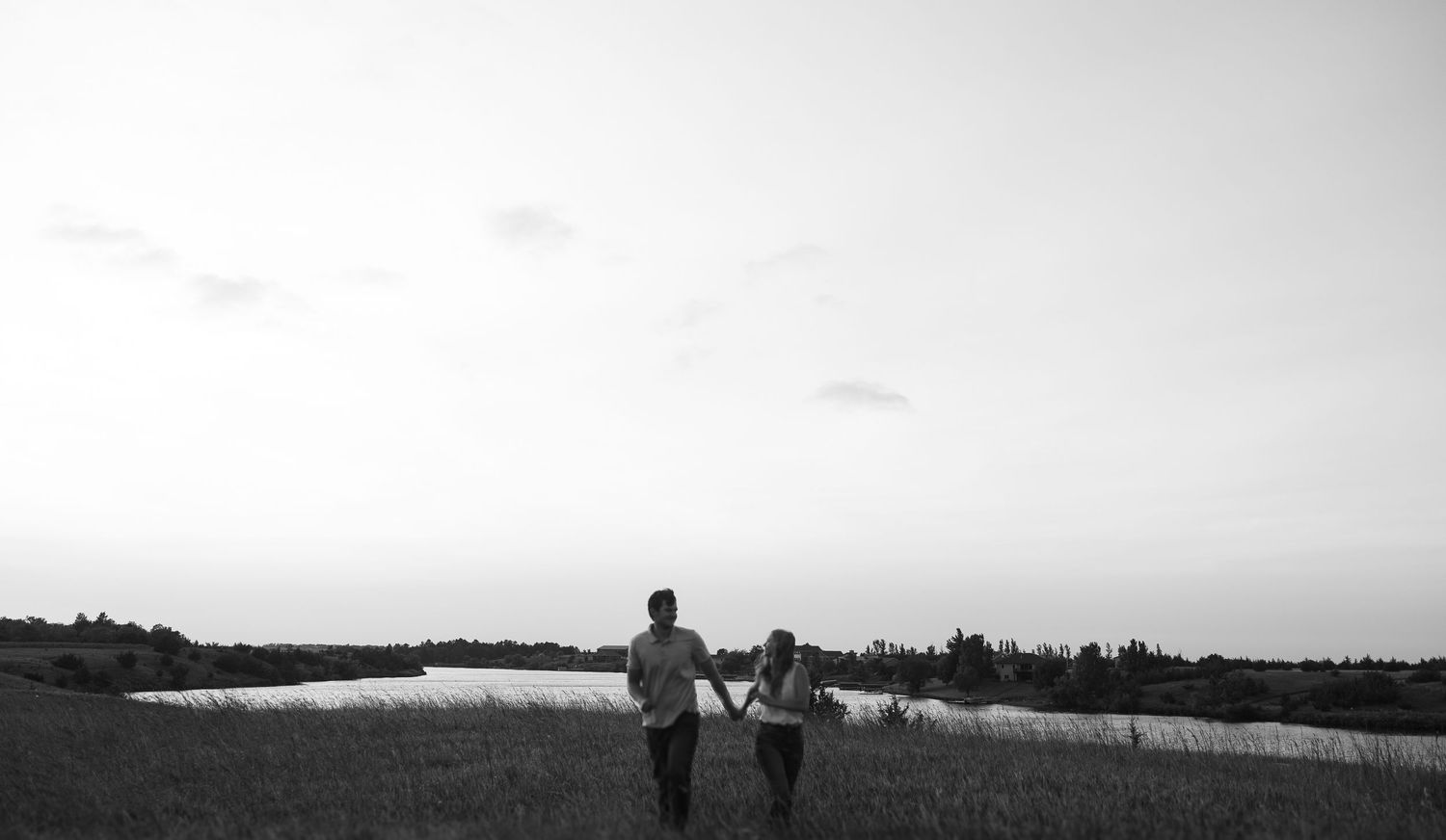 Silhouettes stand together overlooking a tranquil lake landscape in black and white photography. Sioux Falls, South Dakota.