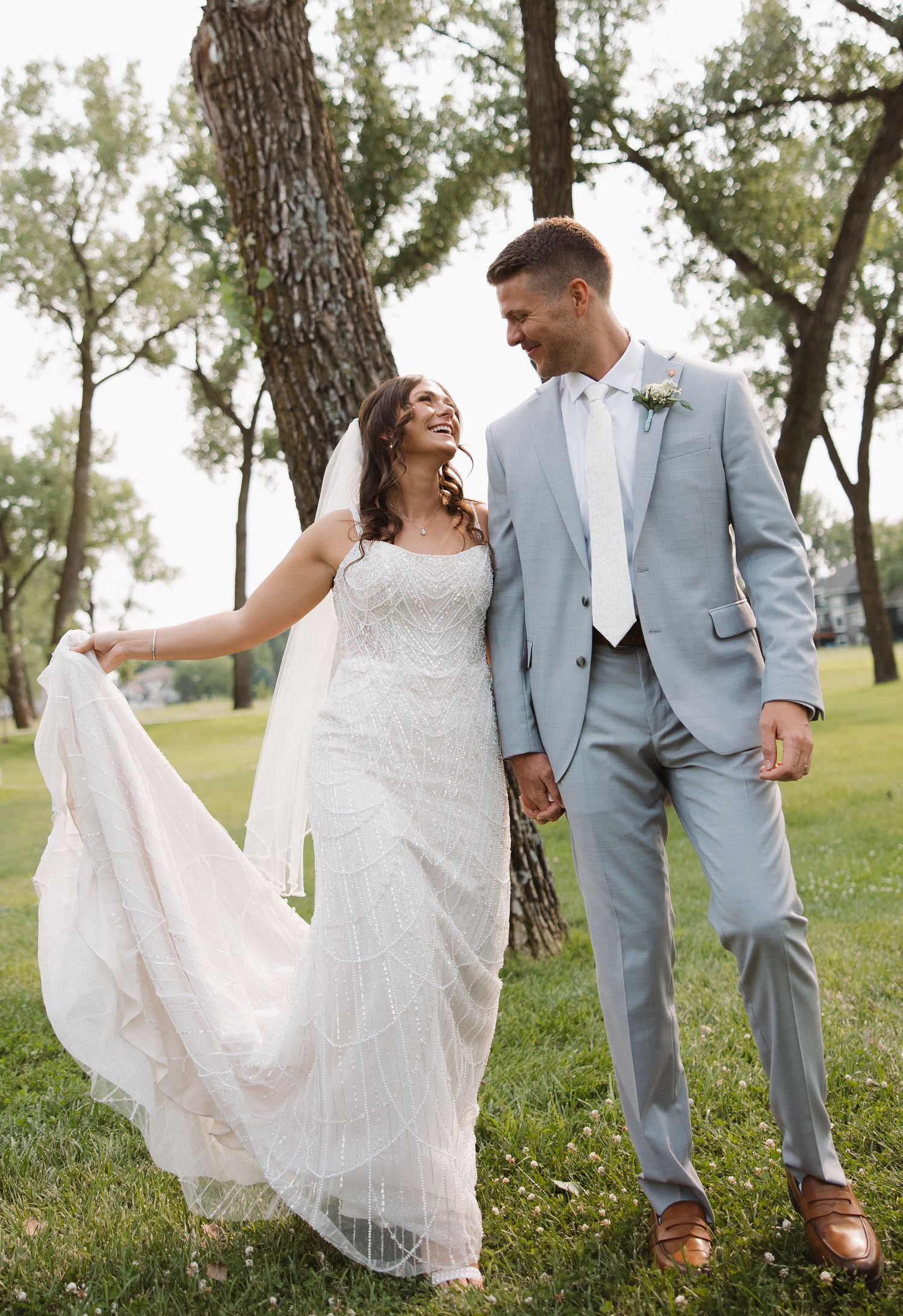 A wedding couple laughs together while walking through a sun-dappled park. Sioux Falls, South Dakota.