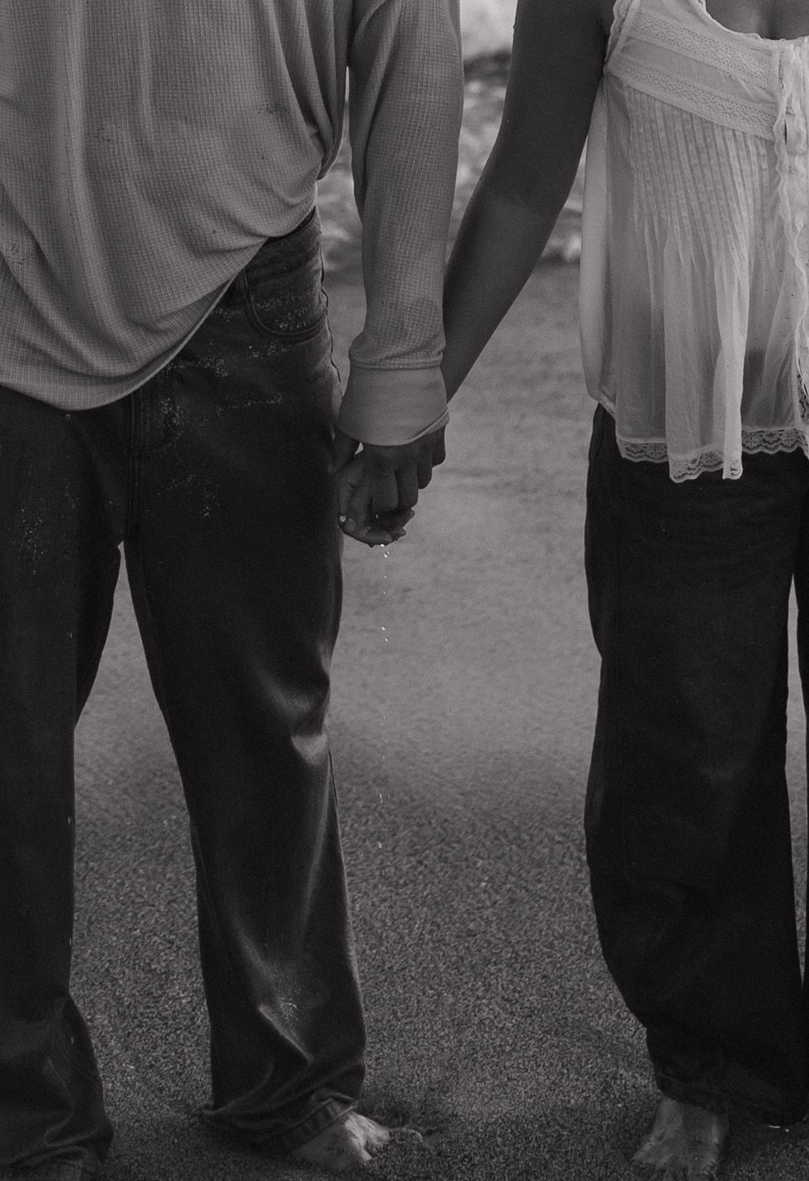 Black and white photo of a couple holding hands while standing barefoot on a wet pavement.