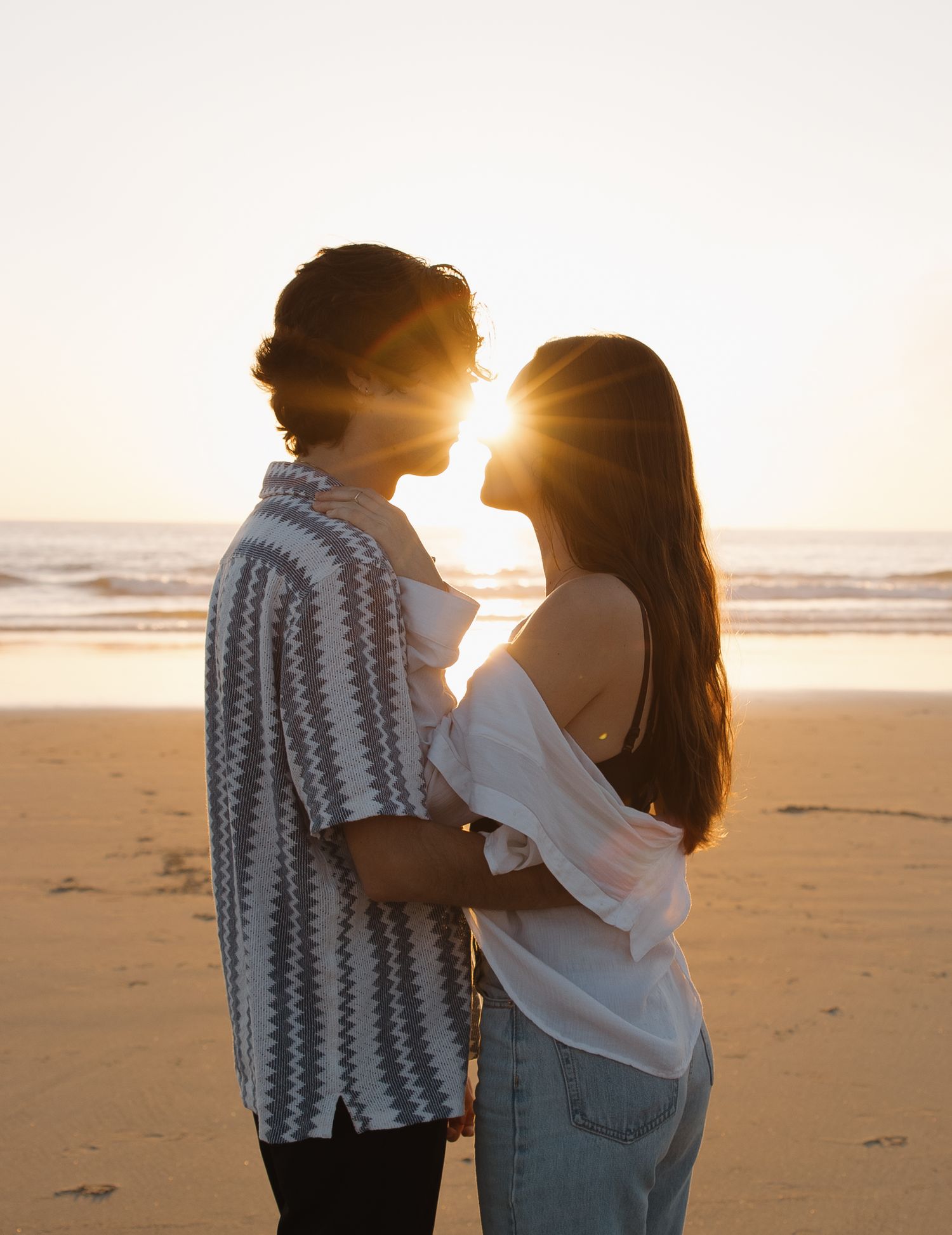 A silhouetted couple shares an intimate moment on the beach at sunset. Sacramento, California. Newport Beach, California.
