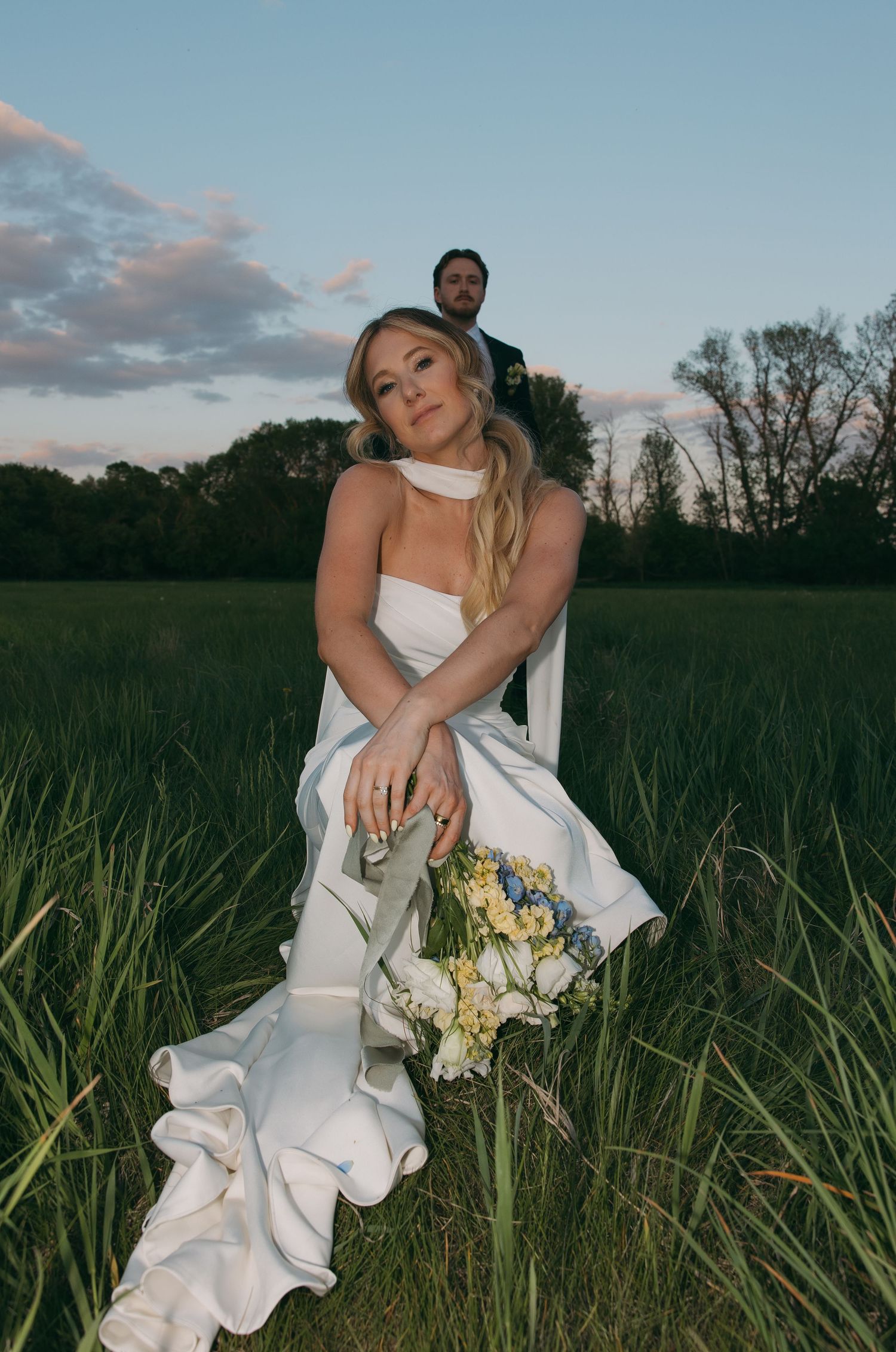 A couple poses in a grassy field at sunset with a bouquet of flowers. Sioux Falls, South Dakota.