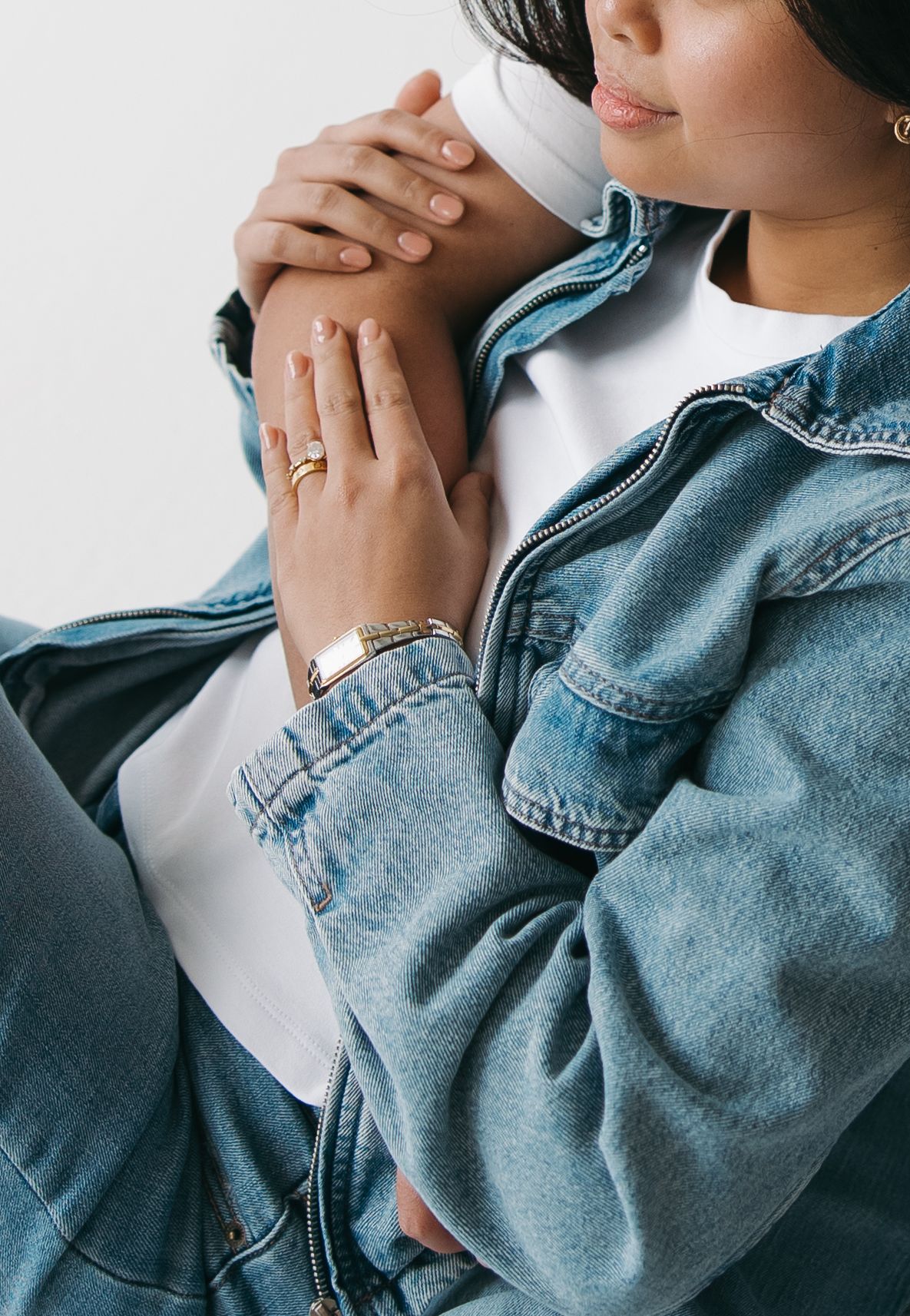 Woman in denim jacket wearing gold ring and bracelet, showcasing elegant jewelry accessories.