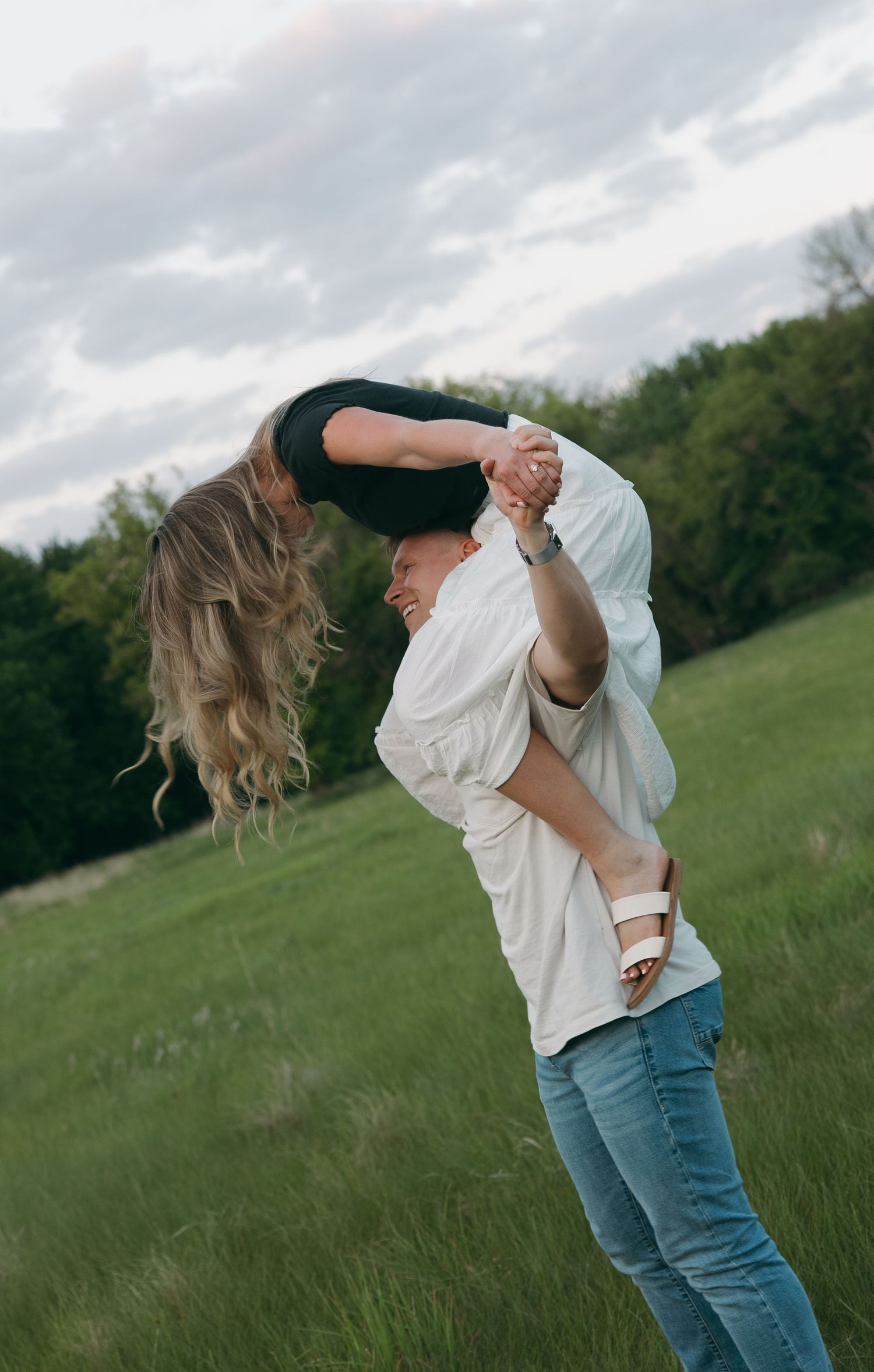A couple dances together on a grassy hillside during sunset with one person dipping the other dramatically.