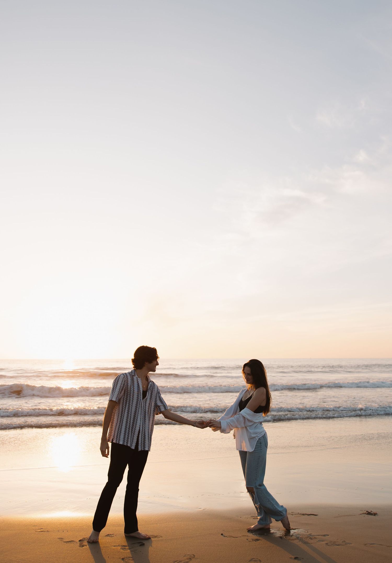 A romantic couple holds hands while dancing on a beach at golden hour. Sacramento, California. Newport Beach, California.