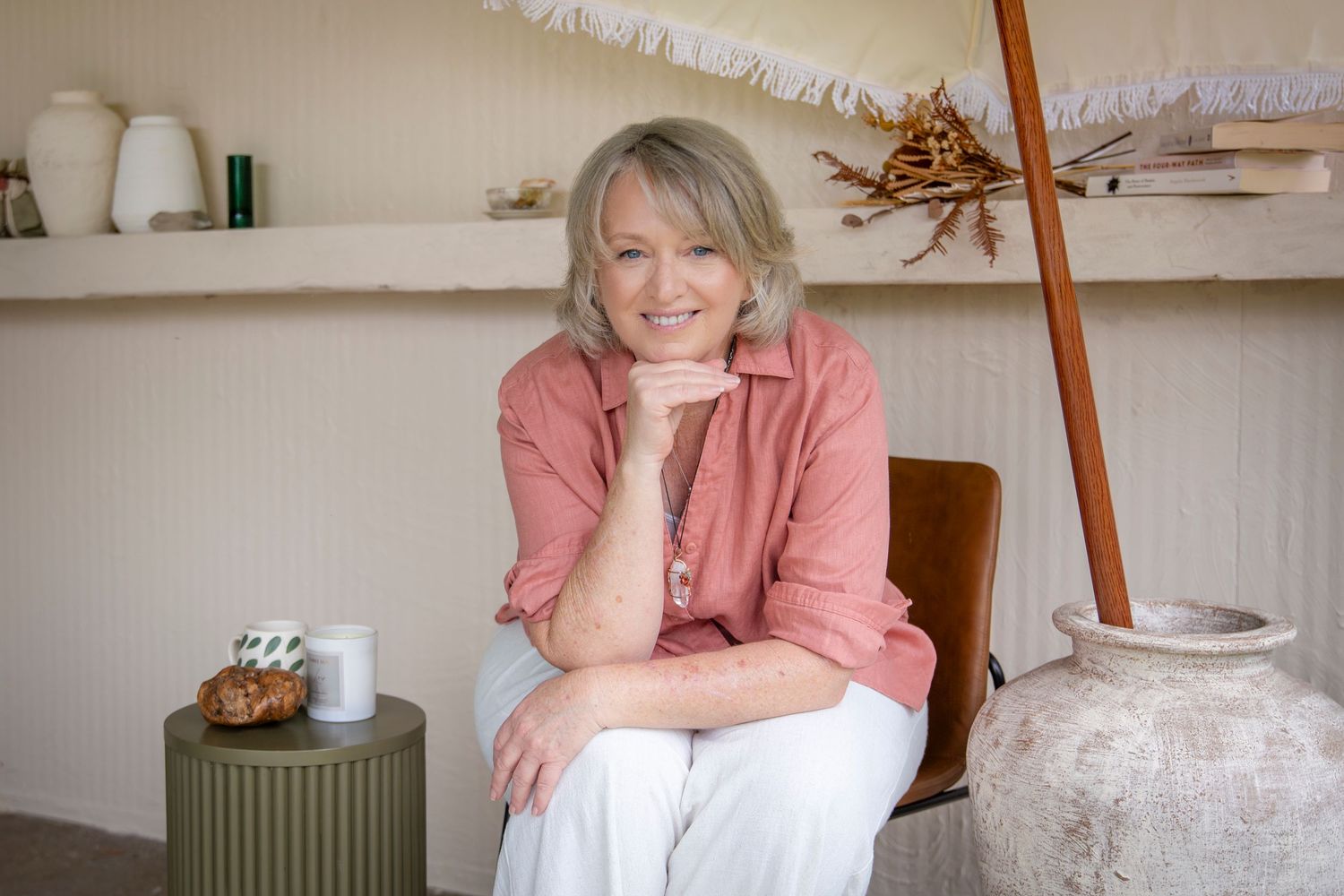 Casual studio portrait of a woman in a pink shirt seated in a modern, neutral-toned setting.