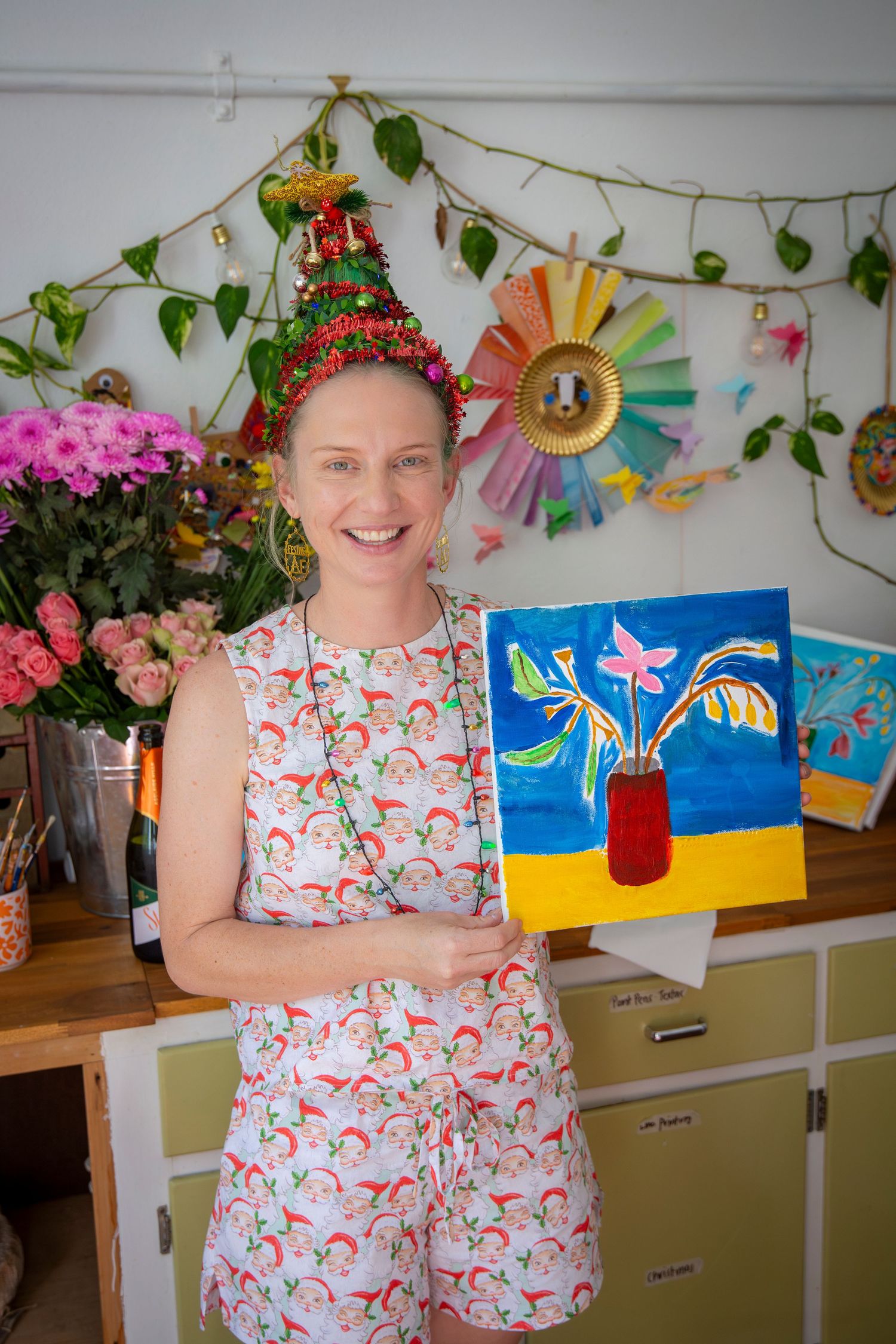Woman wearing Christmas hat proudly holding a colourful painted canvas at a creative Rockhampton event