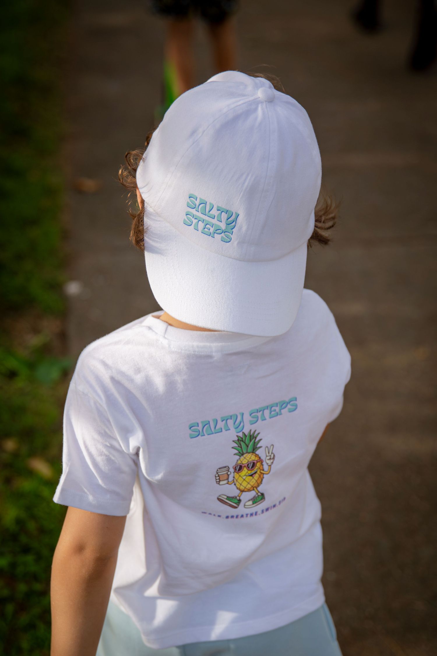 Child in branded Salty Steps shirt walking at beachfront event