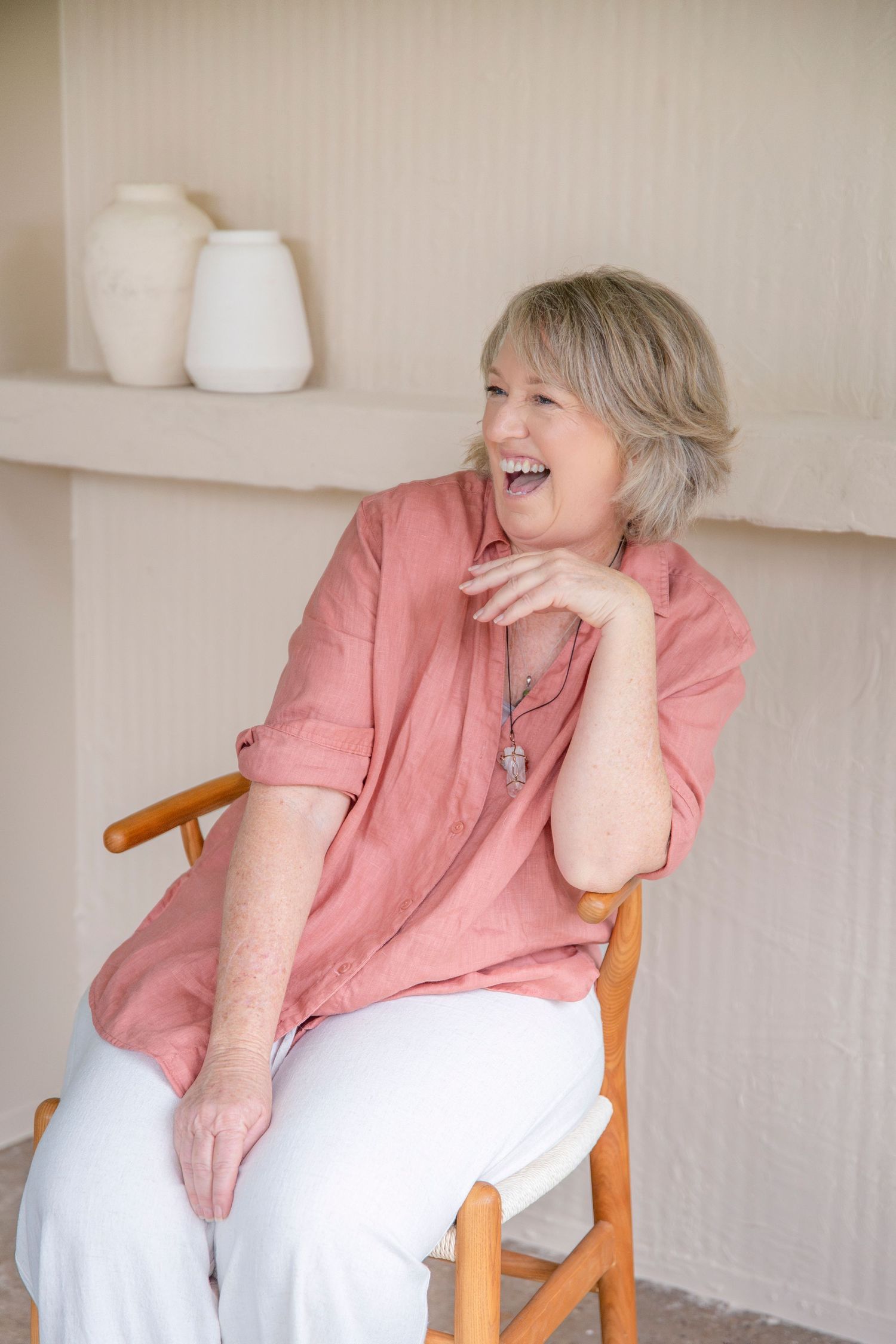 Casual portrait of a woman in a coral shirt smiling on a wooden chair during Rockhampton headshot session