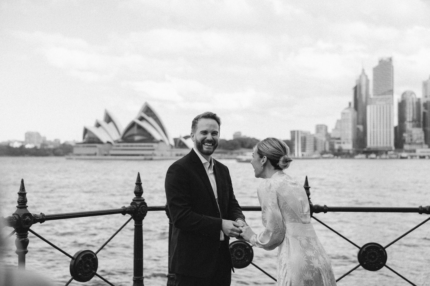 Couple holding hands at Sydney Harbour with Opera House backdrop in black and white wedding photo.