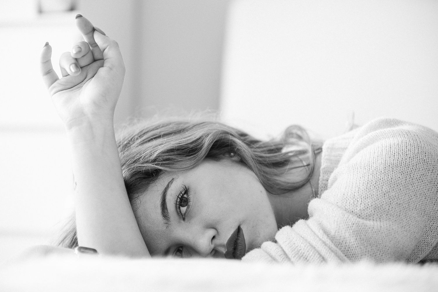 Black and white portrait of someone lying on white bedding in soft natural light.