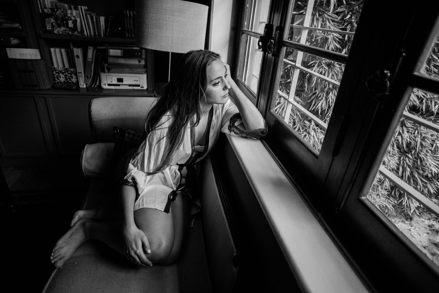 A series of black and white photos showing someone sitting by a window in moody lighting.
