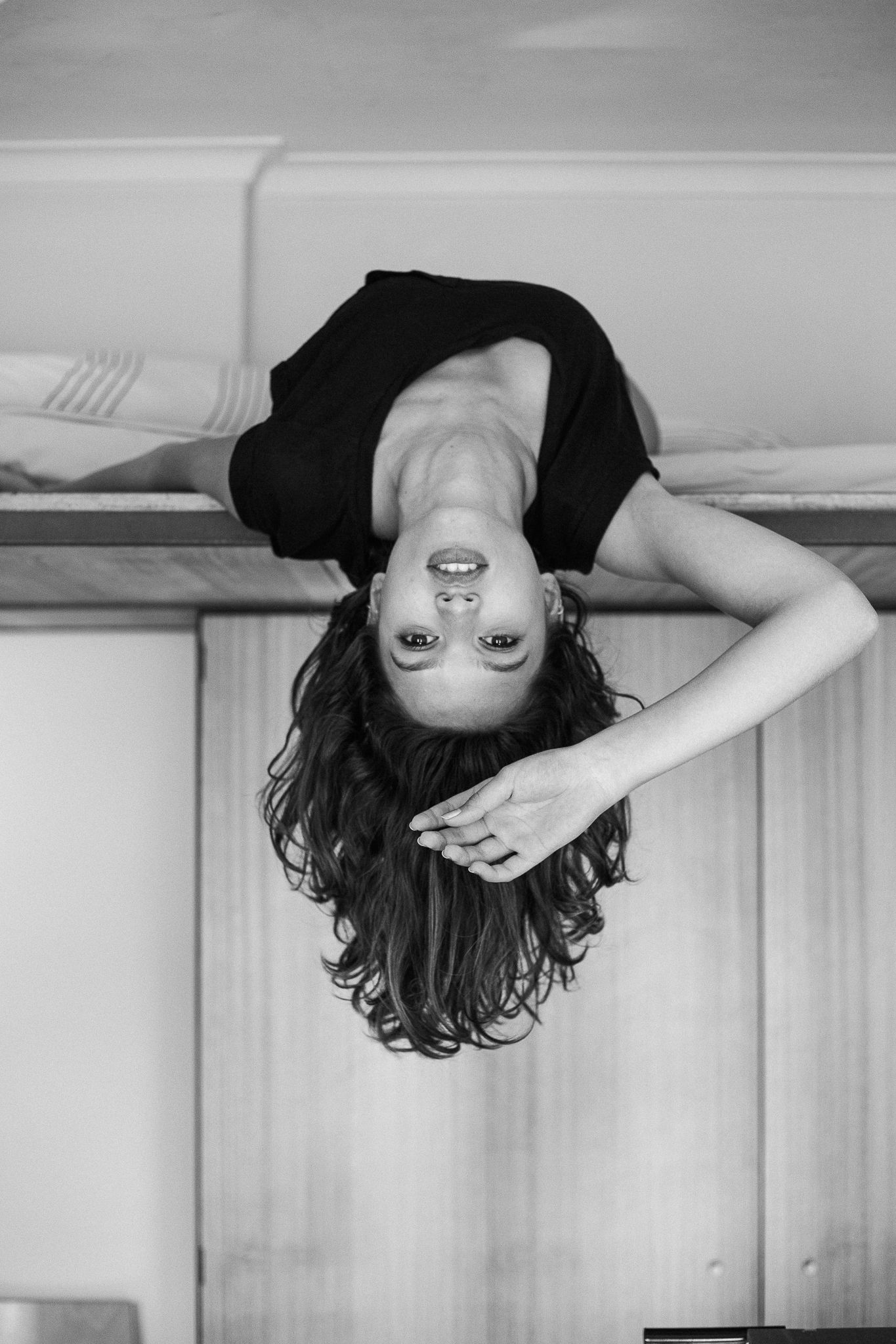A black and white artistic photo sequence showing a person with curly hair hanging upside down against a white wall.