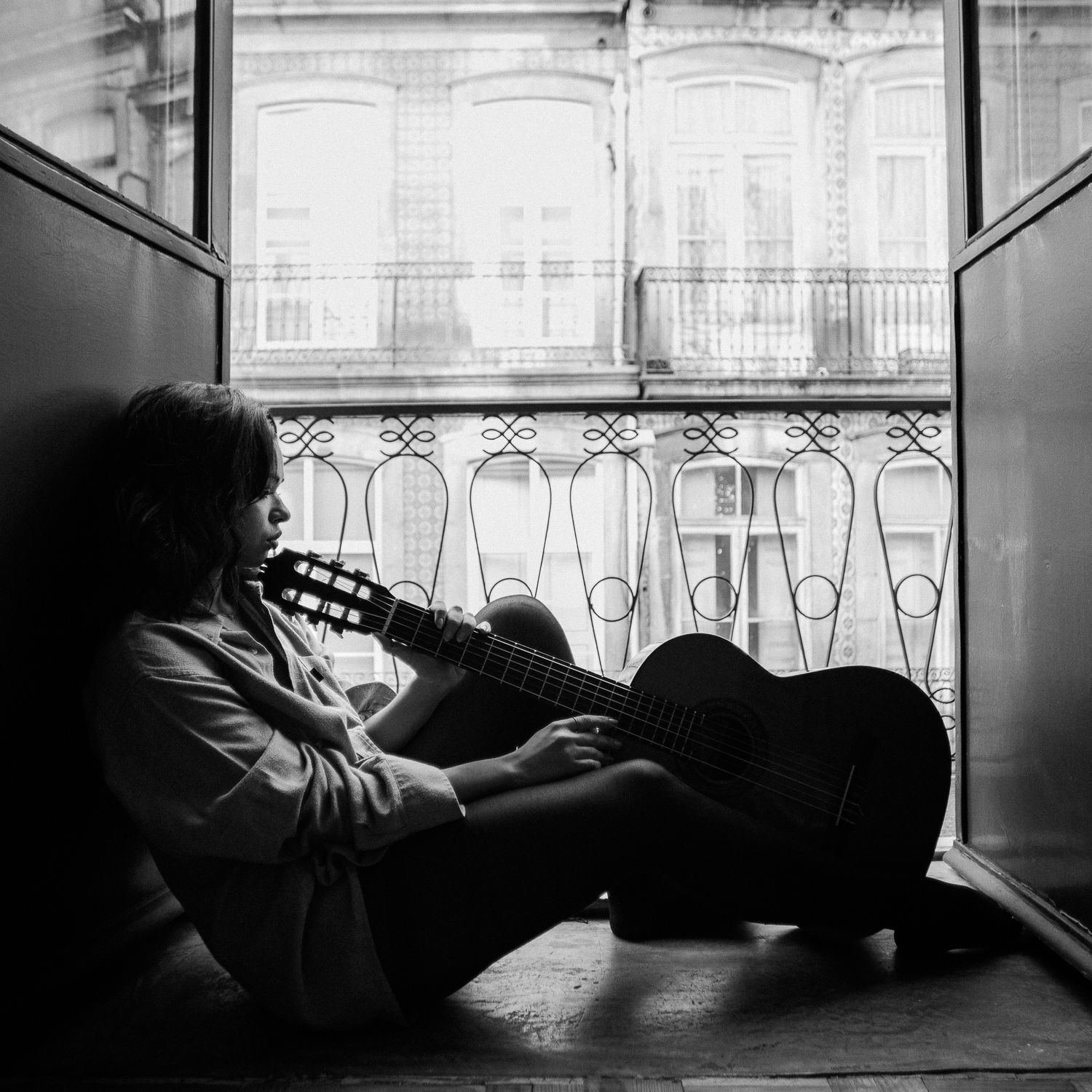 Atmospheric black and white photographs showing a figure resting by a window with ornate railings.