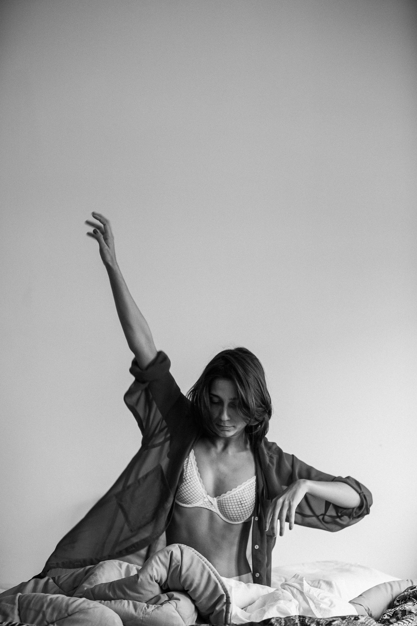 Black and white boudoir photo of figure stretching on bed in morning light.