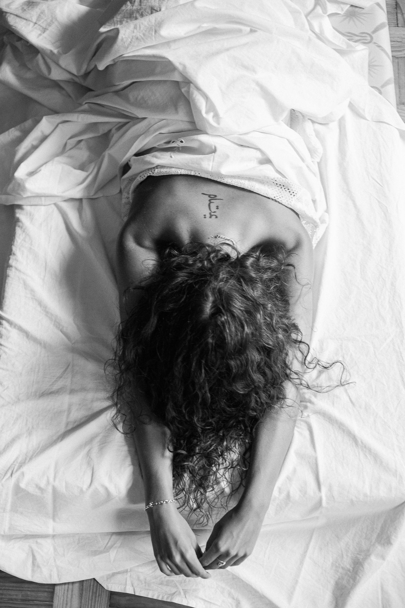 A series of black and white photographs showing a person with curly dark hair lying on white bedding.