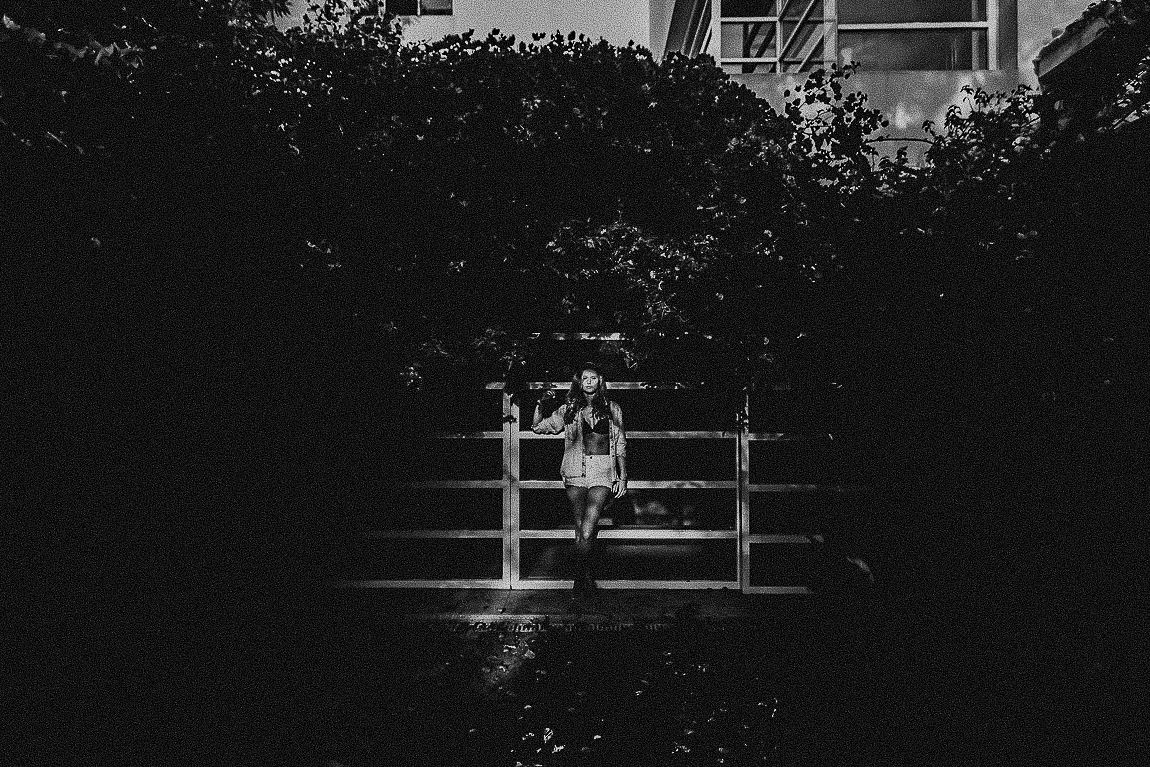 A black and white photograph shows a person walking down a dark hallway with bright windows visible at the end.
