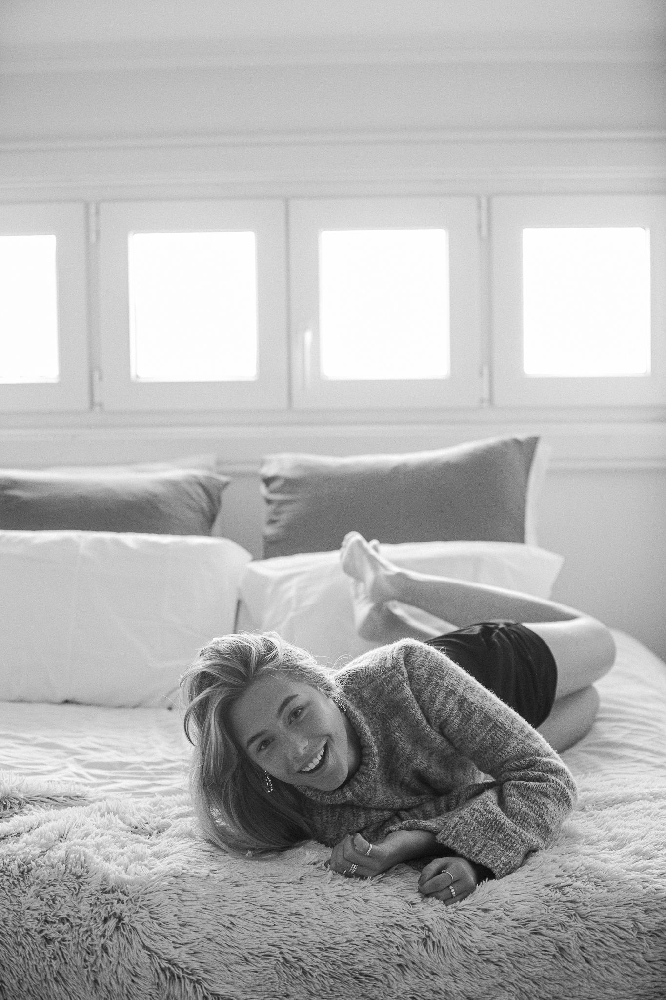 Black and white photo series showing a person relaxing on a soft bed in a bright room with windows.