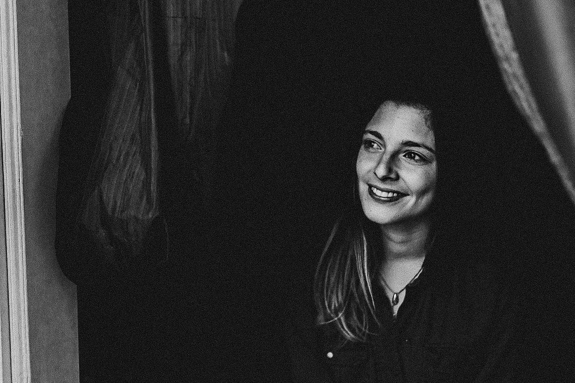 Black and white portrait of someone smiling warmly while standing in a doorway.