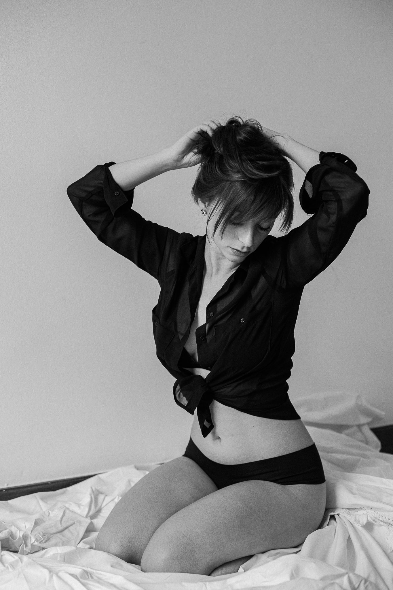 Dramatic black and white boudoir series featuring dark clothing against light background.