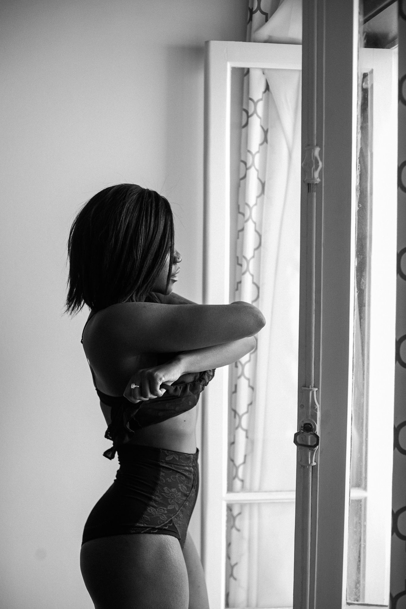 Black and white photo of a person standing by a window in silhouette, creating a dramatic shadow effect.