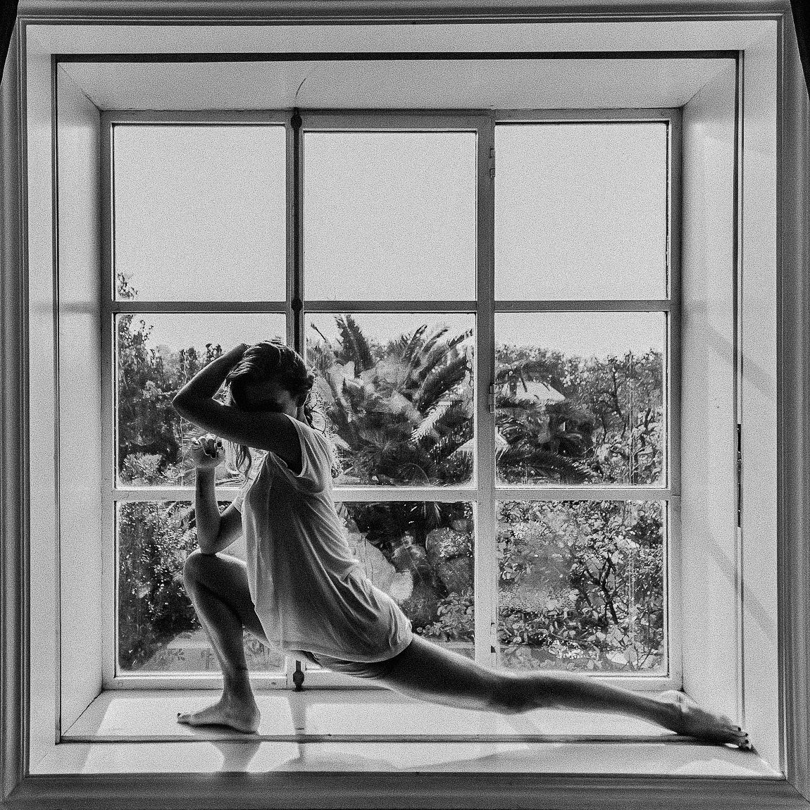 Black and white artistic photograph showing a person in silhouette doing a split pose across three window frames.