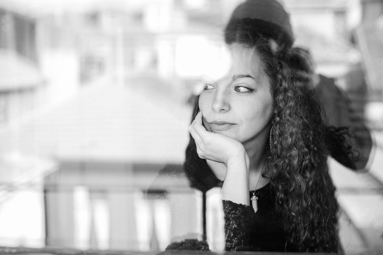 Artistic black and white portrait showing curly hair and contemplative pose against urban backdrop.