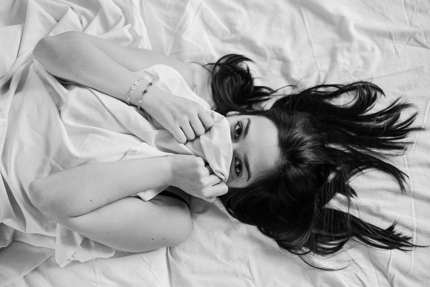 Black and white photo series showing a person with dark hair lying on white sheets in various artistic poses.