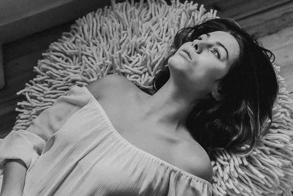 A person lies on a textured white surface in a dramatic black and white photograph.