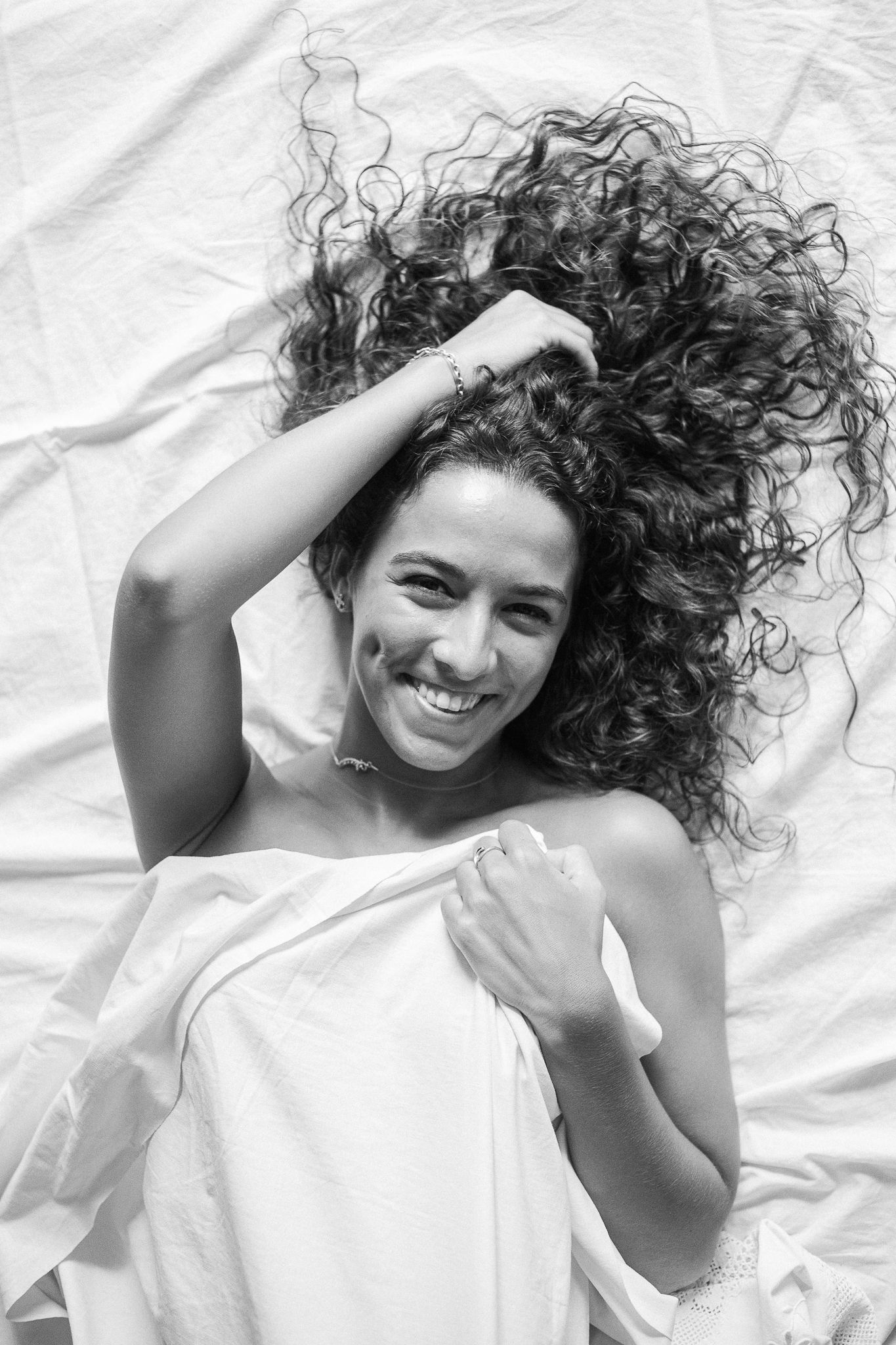 A series of four black and white photos showing someone with curly hair lying on white fabric while smiling and posing.
