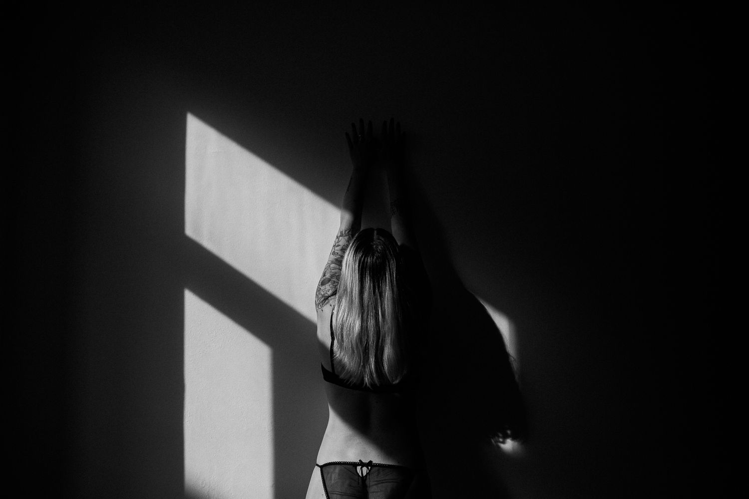 A dramatic black and white silhouette of a person standing in front of a window with stark light casting shadows.