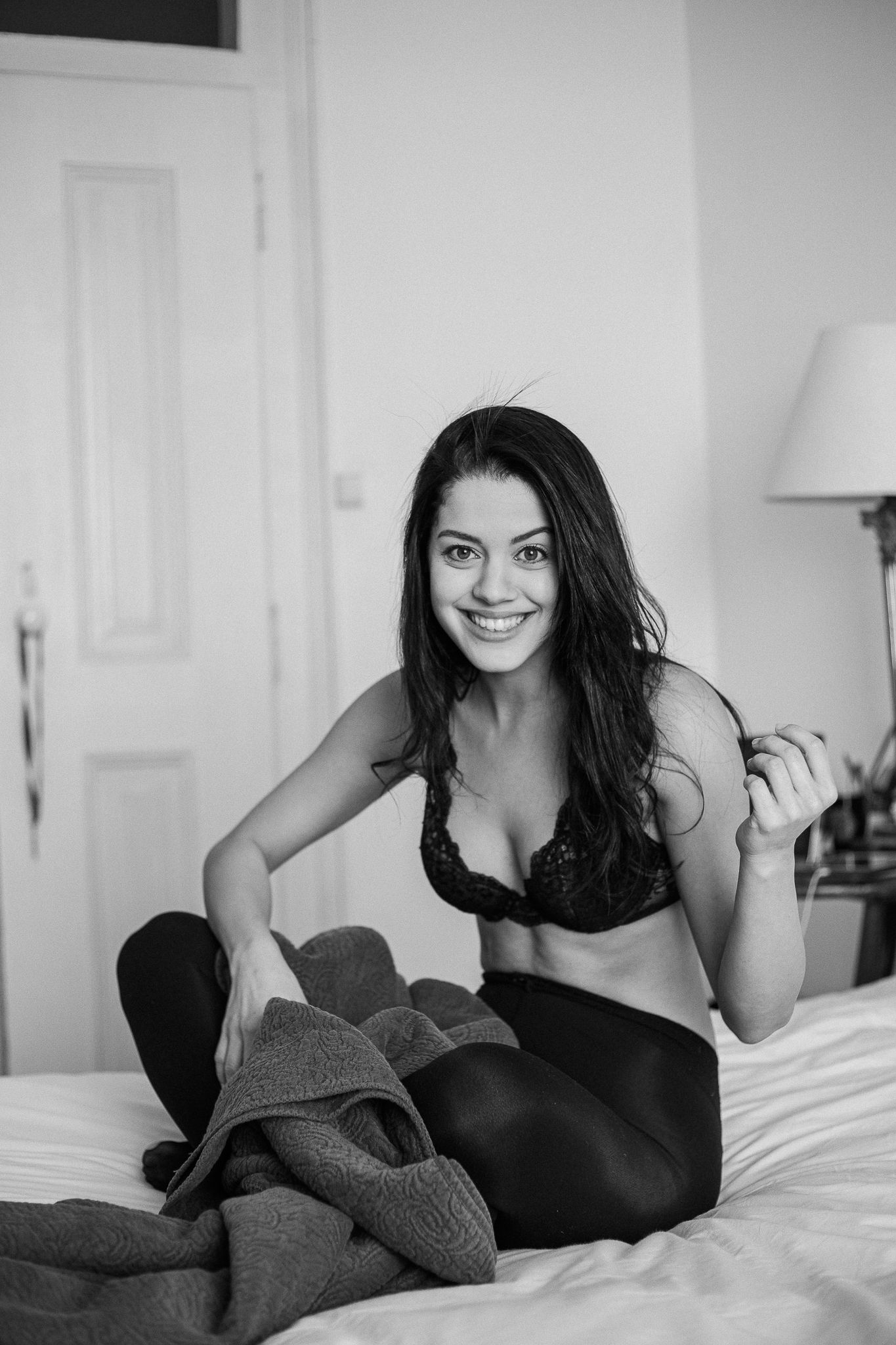Black and white boudoir photo series showing a woman in casual attire relaxing on white bedding.