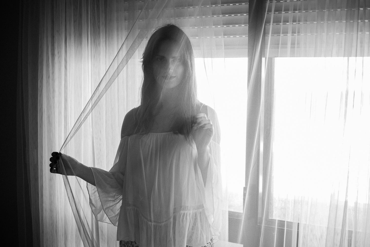 A series of black and white silhouettes against bright window light show a person in flowing fabric moving gracefully.