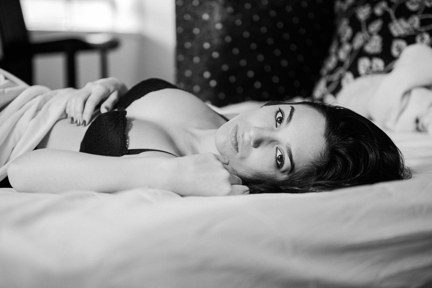 Black and white artistic boudoir photo series showing figure reclining on white bedding.