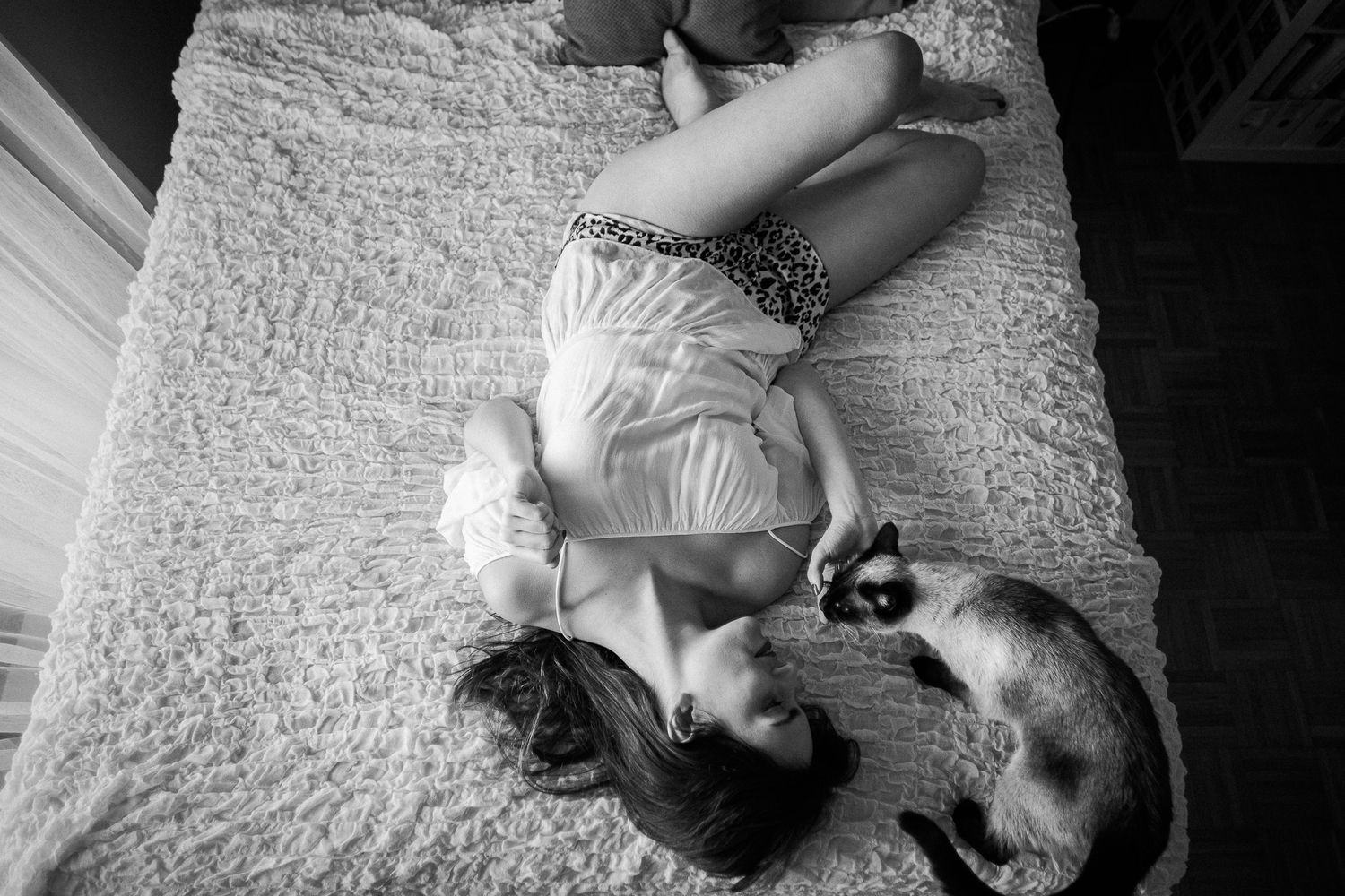 A sequence of black and white photos shows a person lying down with a cat on a textured bedspread.