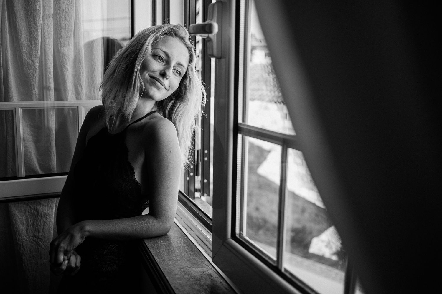 Moody black and white portrait by a window with natural lighting and shadows.