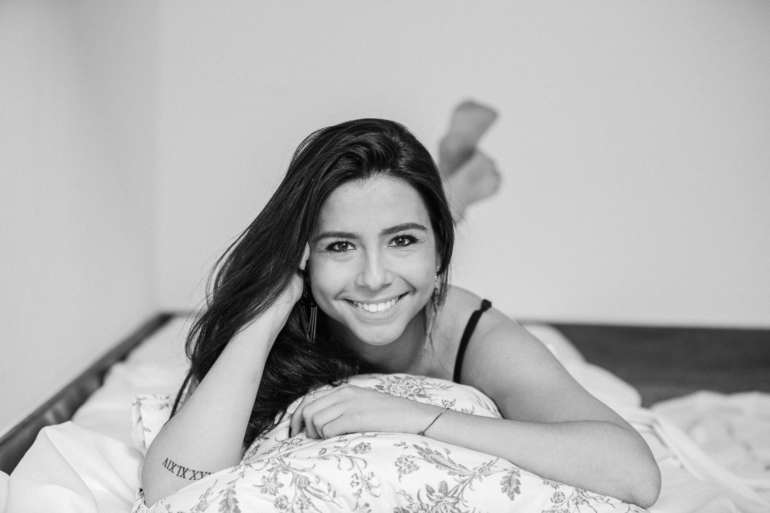 A black and white photo series shows someone posing in lace on a bed with various expressions.