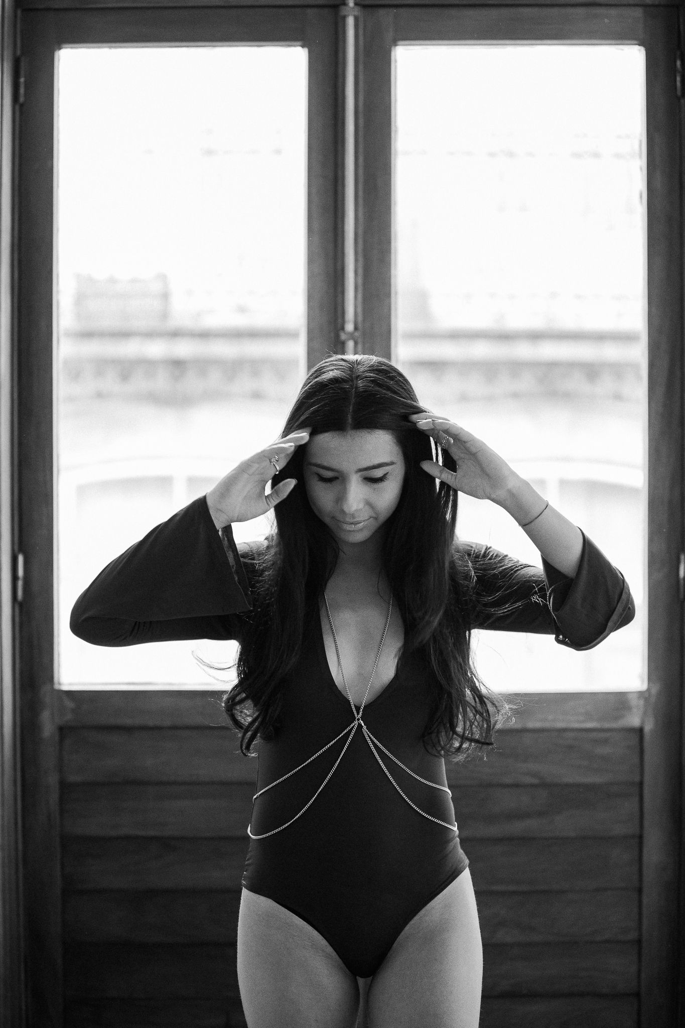 A black and white artistic portrait of a dancer in a leotard practicing movements in front of studio windows.