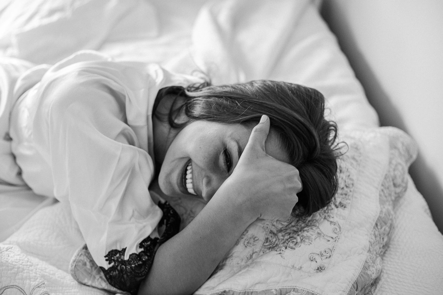 A collection of black and white photos showing a person lying down and smiling on white bedding.